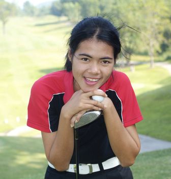 Yeoung, female golf player smiling, holding golf club and ball, with fairway in the background.