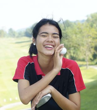 Yeoung, female golf player smiling, holding golf club and ball, with fairway in the background.
