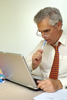 A businessman sits, thoughtful, in front of his laptop computer, sucking the end of his pencil.. Space for text on the white background.
