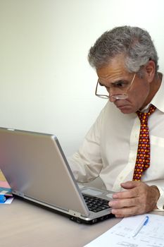 A businessman peers at his laptop computer with intense concentration and a hint of puzzlement. Space for text on the white background.