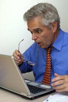 A businessman pulls off his glasses in astonishment as he gazes at the screen of his laptop..