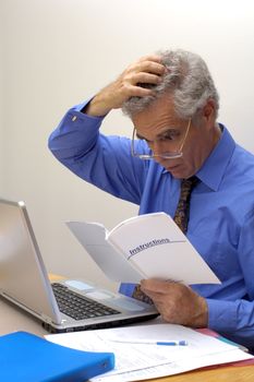 An older businessman gazes at the instruction booklet of his laptop, scratching his head in puzzlement. How does this thing work?