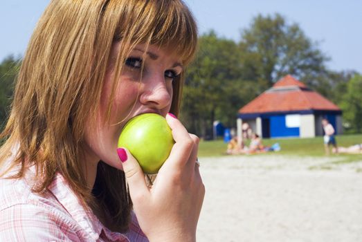Pretty teen eating a healthy green apple on the beach.