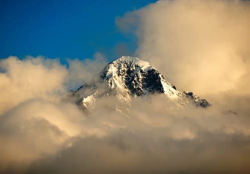 A Mountain peak in Alaska near Matanuska Glacier peaks through the clouds at sunset.