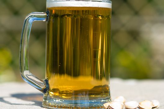 Full mug with beer on a table covered with a cloth and pistachios. Closeup