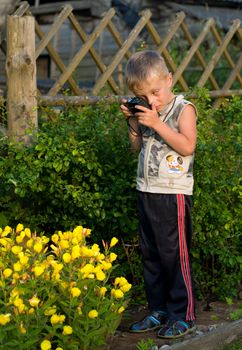 The little boy photographs flowers on a summer residence.