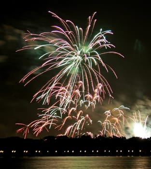 Fireworks in the dark sky over a lake.