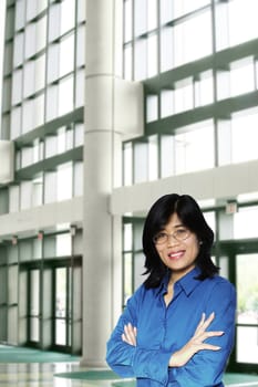 Confident asian business woman standing arms crossed inside large office complex