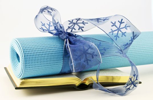 Serene blue yoga mat wrapped with blue ribbon placed with open book; fitness, study, and yoga are gifts of healthy lifestyle.  