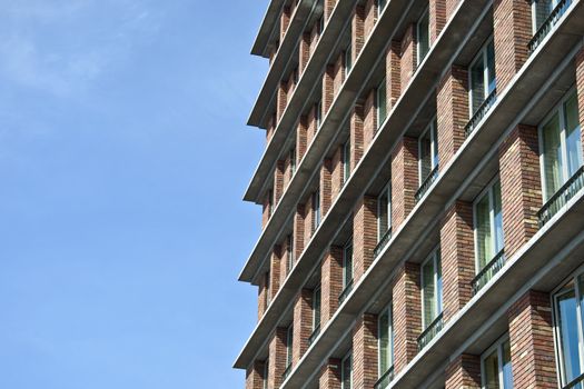 Fragment of the facade of the modern brick residential house with the same balcony. Detail. Against the blue sky.