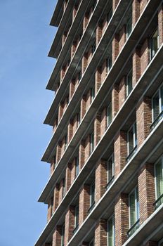 Fragment of the facade of the modern brick residential house with the same balcony. Detail. Against the blue sky.