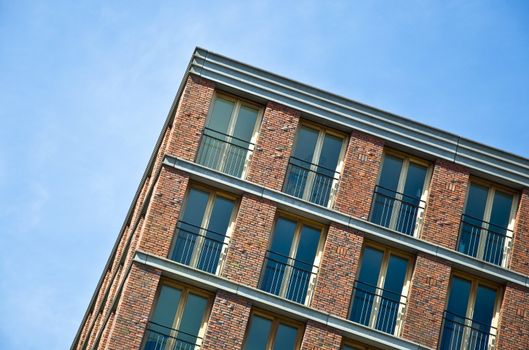 Fragment of the facade of the modern brick residential house with the same balcony. Detail. Against the blue sky.