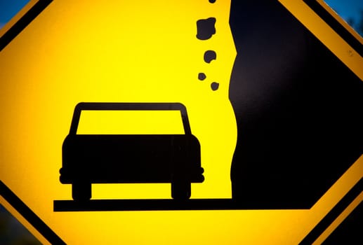 Close-up of a yellow sign with a car silhouette and falling rocks