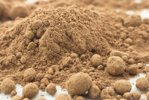 Macro (close-up) of cocoa powder, scattered on white surface and forming the shape of a mountain.  Some powder has beaded and formed into balls.