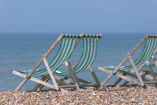 Green and white striped wooden deckchairs, facing the sea on a pebble beach.  Sunny day.