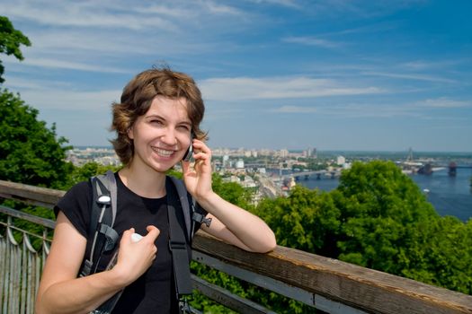 Young woman smiling and talking on the phone at beautiful backdrop of the city of Kyiv