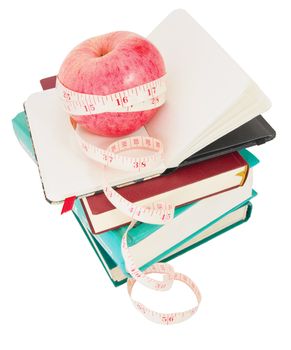 Big ripe red apple with white measure tape around it on pile of books as metaphor of healthy eating and diet