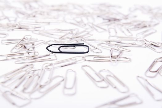 One black paperclip among many steel grey paperclips on white background