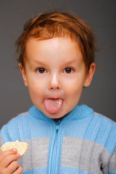 Portrait of a little boy in a blue sweater with a cookie showing his tongue