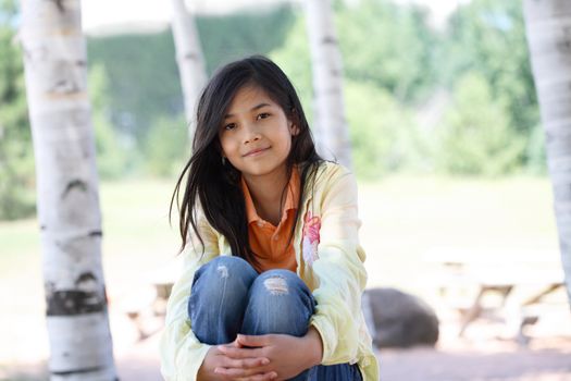 Little girl sitting under birch trees