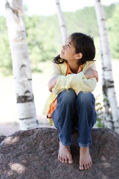 Little girl sitting under trees, looking up