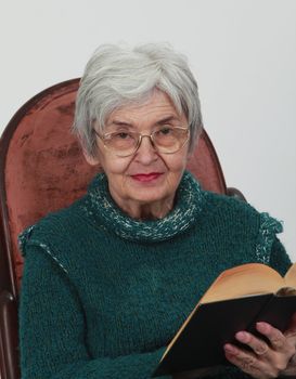 Portrait of an old woman with a black book against a grey background.