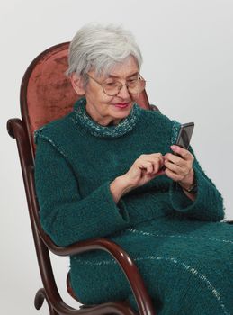 Close up image of a senior woman siting in a rocker and writing a phone message.