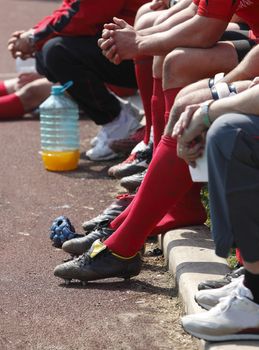 Image of sportive's legs and hands on a substitutes bench.They are rugby players.