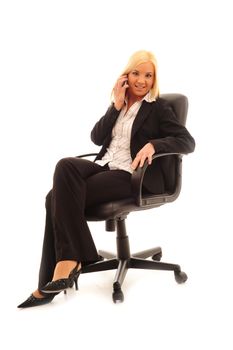 Young confident business woman with blonde hair in a stylish dark suit, sitting on a leather chair on a white background.