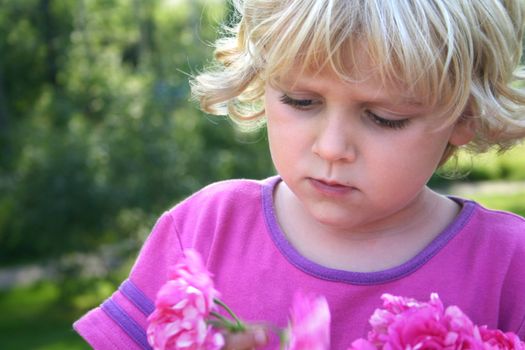 A blond serious little girl in a garden, looking at pions. Horizontal