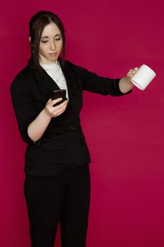 Young business woman flipping her cup of coffee and working off her smart phone against pink background