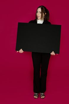 Young business woman wearing a business suit standing behind a black board against pink background