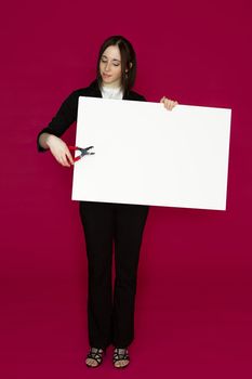 Young business woman holding a pair of pliers pointing to a white board against pink background