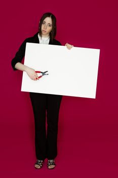 Young business woman holding a pair of pliers pointing to a white board with sad expression against pink background