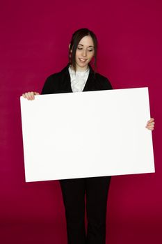 Young business woman wearing a business suit standing behind looking down at a white board against pink background