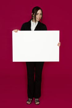 Smiling young business woman wearing a business suit standing behind looking down at a white board against pink background