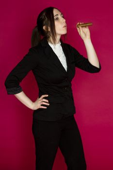 Young woman in a business suit blowing smoke from a cigar against a pink background