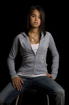 Teen girl sitting on a stool starring in the distance against a black background