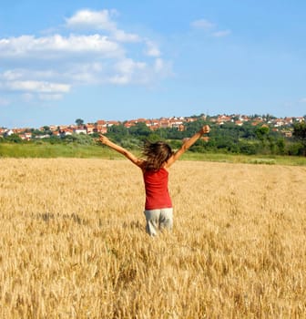 happy girl jumping in yellow wheat field at scenic rural background