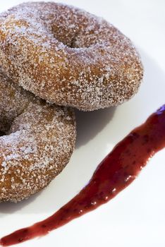 A pair of cinnamon donuts garnished with rasberry sauce.