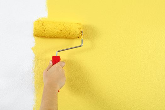 Photo of a female painting a wall with a roller and yellow paint.