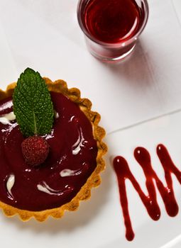 A Raspberry tart garnished with a fresh raspberry and mint accompanied by a raspberry shot.