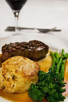 A perfectly grilled steak served with broccolini and a potato cake with gravy and red wine.