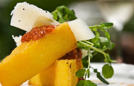 A serving of polenta with a tomato sauce, cheese and watercress, served with a glass of white wine.