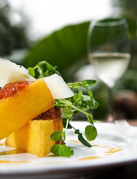 A serving of polenta with a tomato sauce, cheese and watercress, served with a glass of white wine.