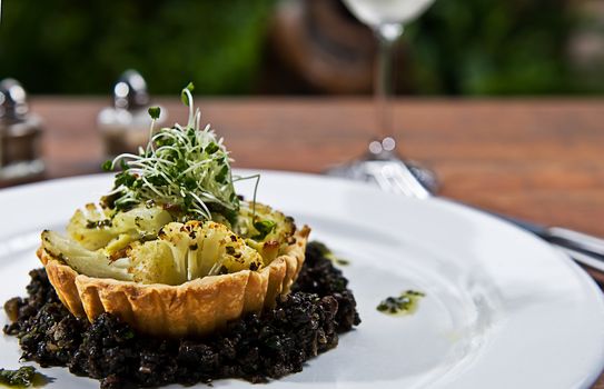 A tart made of cauliflower in a pastry shell, on a bed of mushrooms and herbs.