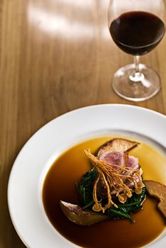 Crispy duck on a bed of spinach served with red wine in a restaurant.