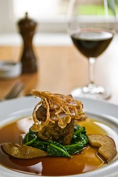 Crispy duck on a bed of spinach served with red wine in a restaurant.