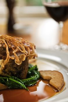 Crispy duck on a bed of spinach served with red wine in a restaurant.