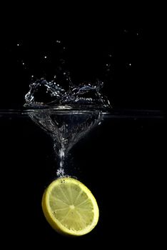 A lemon dropped into water creating a splash and bubbles. Isolated on black.